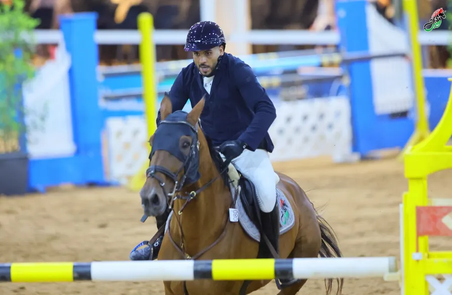 Rider guiding a bay horse past the yellow poles in the arena